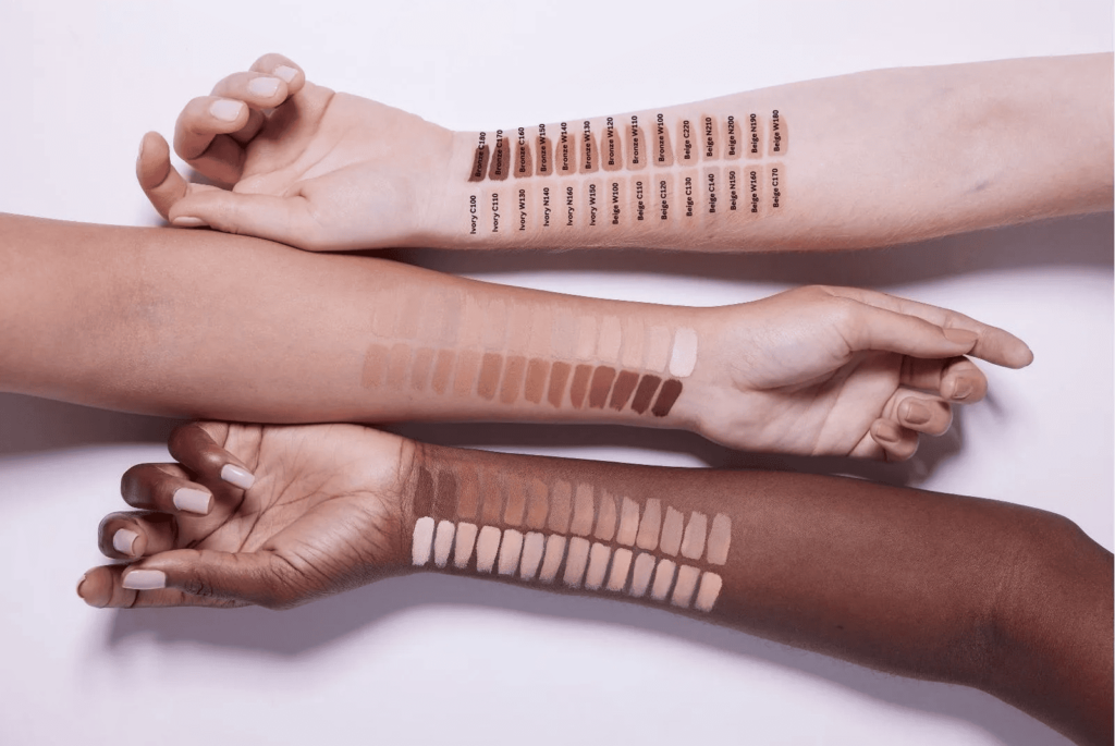 Fotografia com todos os tons de base Mary Kay Timewise disponíveis, em swatches nos braços de três moças de pele clara, média e escura.