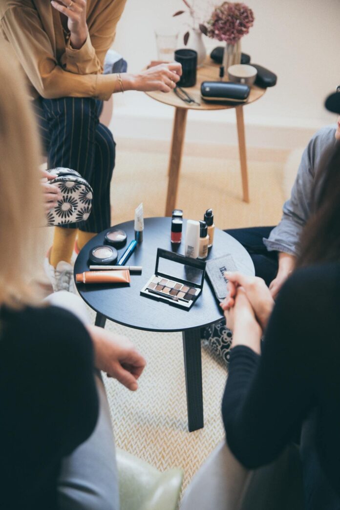 Fotografia de mesa com maquiagens e mulheres ao redor, utilizada para ilustrar artigo sobre a maquiagem mary kay.