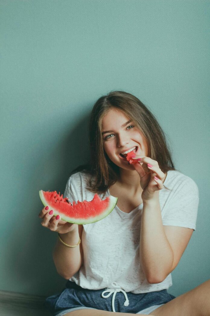 Fotografia de moça comendo melancia, utilizada para ilustrar artigo sobre vitamina para pele.